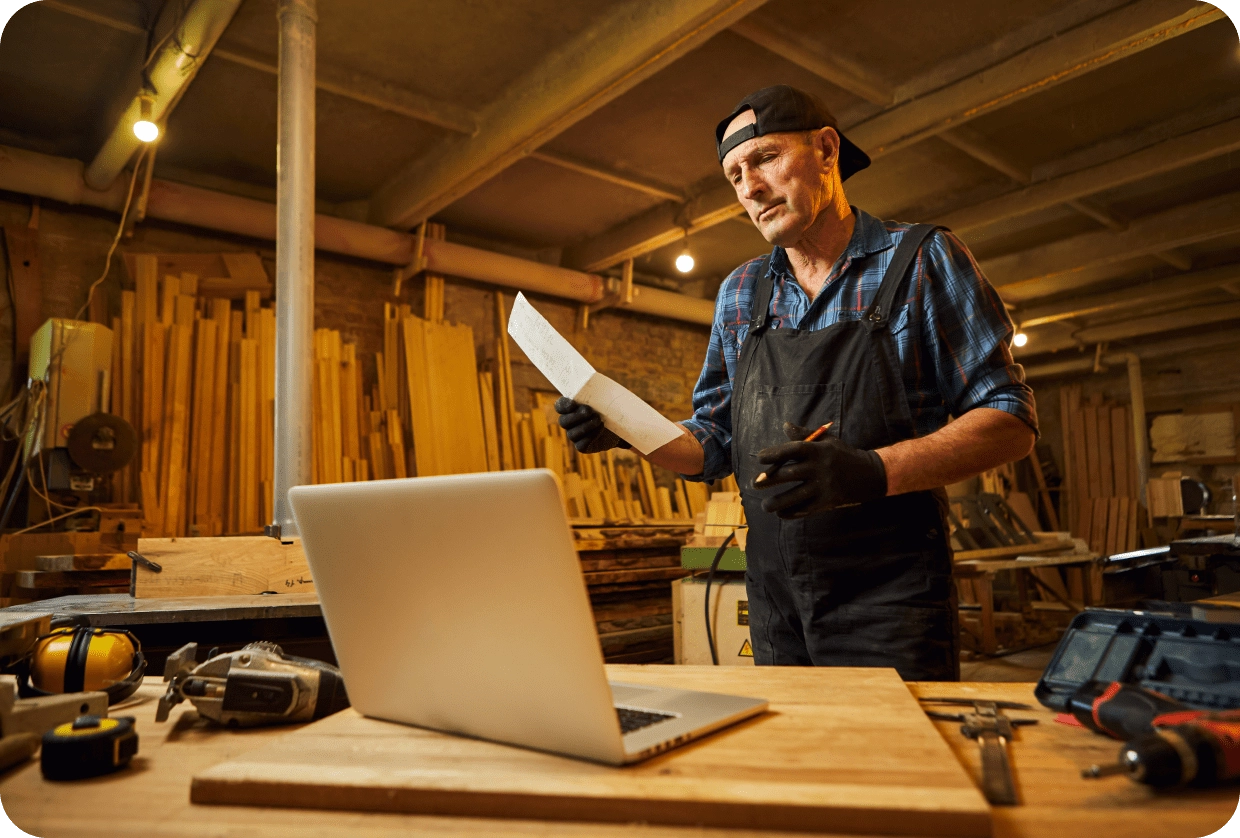 A tradesperson in a workshop using a laptop.