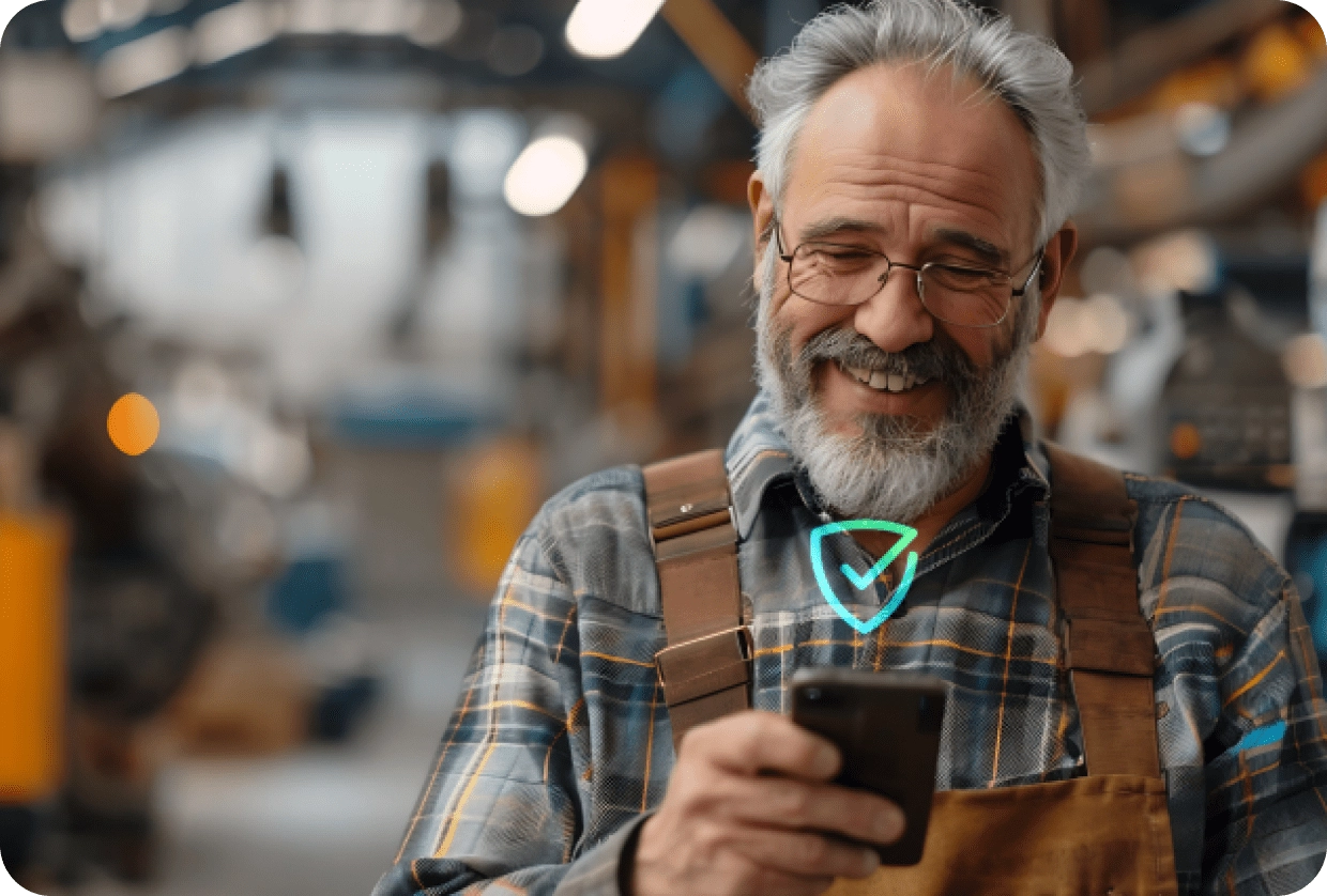 Smiling older craftsman in overalls using a smartphone in a workshop.